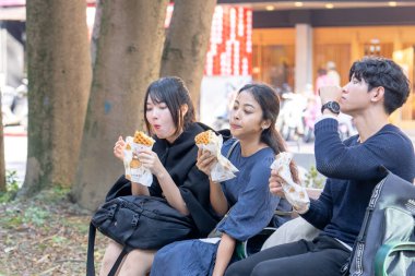 Tayvanlı bir kadın, Tayvanlı bir erkek ve Asyalı bir kadın, Taipei 'de Daan Bölgesi' nde bir bankta oturmuş, büyük bir waffle 'ın keyfini çıkarıyorlar..