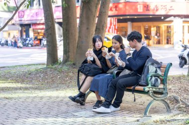 Tayvanlı bir kadın, Tayvanlı bir erkek ve Asyalı bir kadın, Taipei 'de Daan Bölgesi' nde bir bankta oturmuş, büyük bir waffle 'ın keyfini çıkarıyorlar..