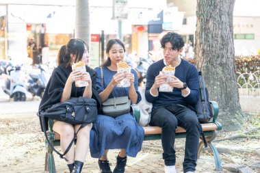 Tayvanlı bir kadın, Tayvanlı bir erkek ve Asyalı bir kadın, Taipei 'de Daan Bölgesi' nde bir bankta oturmuş, büyük bir waffle 'ın keyfini çıkarıyorlar..