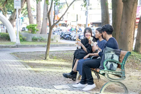 Tayvanlı bir kadın, Tayvanlı bir erkek ve Asyalı bir kadın, Taipei 'de Daan Bölgesi' nde bir bankta oturmuş, büyük bir waffle 'ın keyfini çıkarıyorlar..