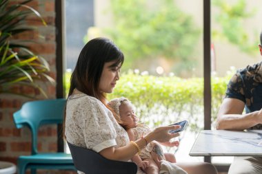 30 'lu yaşlarda Hintli bir Malezyalı erkek ve 20' li yaşlarında bir kadın birkaç aylık bebeklerini güneşli bir yaz öğleden sonrasında Malezya 'nın Selangor kentindeki şık bir kafede tutuyorlar..