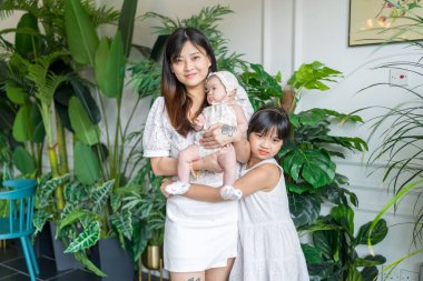 20 'li yaşlarda Malezyalı bir kadın, altı yaşında bir kız ve birkaç aylık bir bebek güneşli bir yaz öğleden sonra Selangor, Malezya' da şık bir kafede çiçeklerin önünde birbirlerine sokuluyorlar.