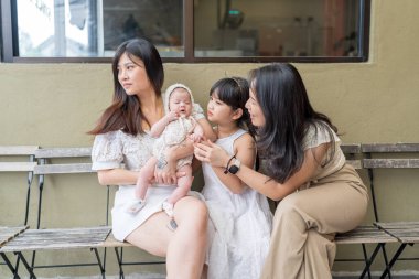 20 'li yaşlarda Malezyalı bir kadın kucağında birkaç aylık bir bebek, altı yaşında bir kız ve 20' li yaşlarda Malezyalı bir kadın Selangor, Malezya 'da şık bir kafede birlikte vakit geçiriyorlar.