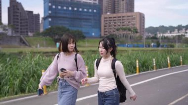 Tayvan 'ın Taipei şehrinde Wenshan Bölgesi' nde bir üniversite kampüsünde yirmili yaşlarının başında yürüyen ve dostça sohbet eden iki genç Tayvanlı kadının yavaş çekim videosu..