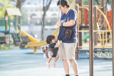 Malezya 'nın Kuala Lumpur Şehir Merkezi' ndeki KLCC Parkı 'nda otuz küsur yaşındaki babasıyla salıncakta sallanan bir Çinli kız çocuğu..