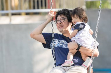 Malezya 'nın Kuala Lumpur Şehir Merkezi' ndeki KLCC Parkı 'nda otuz küsur yaşındaki babasıyla salıncakta sallanan bir Çinli kız çocuğu..