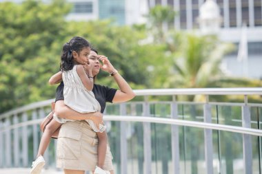 Mini etek giyen 30 yaşlarında Hintli bir anne ve beyaz elbiseli 5 yaşındaki kızı, Malezya 'nın başkenti Kuala Lumpur' da bir köprüde neşeyle vakit geçiriyorlar..