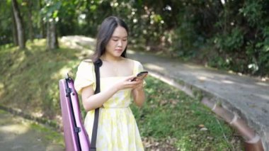 20 'li yaşlarda, sarı elbiseli Çinli bir kadın Malezya' nın Kuala Lumpur yakınlarındaki Bukit Jalil 'deki büyük doğa dolu bir parkın ormanına bakıyor. (Ağır çekim video)