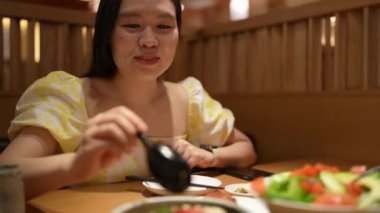 20 'li yaşlarda sarı elbiseli Çinli bir kadın Malezya' nın Kuala Lumpur yakınlarındaki Bukit Jalil 'deki büyük bir alışveriş merkezinde Japon mutfağında Japon mutfağı yiyor..