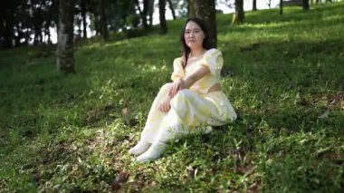 20 'li yaşlarda, sarı elbiseli Çinli bir kadın Malezya, Kuala Lumpur yakınlarındaki Bukit Jalil' deki büyük doğa dolu bir parkın ormanına bakıyor..