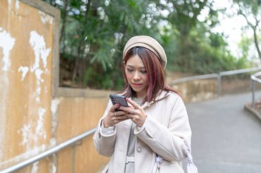 Hong Kong 'lu, kızıl saçlı bir kadın akıllı telefonunu Kowloon Park' ta kullanıyor. Tsim Sha Tsui, Kowloon Adası, Hong Kong..