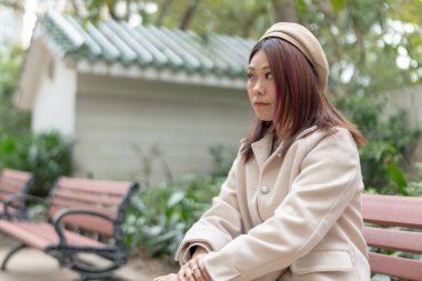 Hong Kong 'daki Kowloon Park, Tsim Sha Tsui, Kowloon Adası, Hong Kong' da büyük bir çeşmenin yanındaki bankta oturan kızılımsı kahverengi saçlı otuz yaşlarında bir kadın..