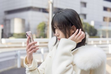 Minato, Tokyo, Japonya 'da umumi bir yolda akıllı telefonunu kullanan yirmili yaşlarda, siyah saçlı, tüylü beyaz önlüklü ve beyaz etekli bir Çinli kadın..