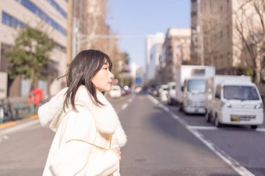 20 'li yaşlarda, siyah saçlı, beyaz önlüklü, tüylü ve beyaz etekli bir Çinli kadın. Minato, Tokyo, Japonya' da halka açık bir yolda yürüyor..