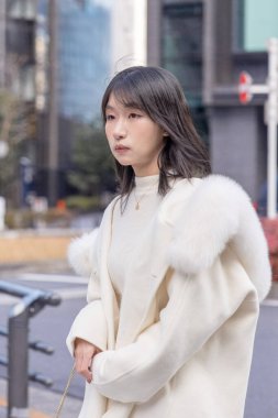 20 'li yaşlarda, siyah saçlı, beyaz önlüklü, tüylü ve beyaz etekli bir Çinli kadın. Minato, Tokyo, Japonya' da halka açık bir yolda yürüyor..