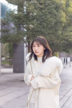 20 'li yaşlarda, siyah saçlı, beyaz önlüklü, tüylü ve beyaz etekli bir Çinli kadın. Minato, Tokyo, Japonya' da halka açık bir yolda yürüyor..