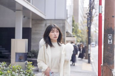 20 'li yaşlarda, siyah saçlı, beyaz önlüklü, tüylü ve beyaz etekli bir Çinli kadın. Minato, Tokyo, Japonya' da halka açık bir yolda yürüyor..