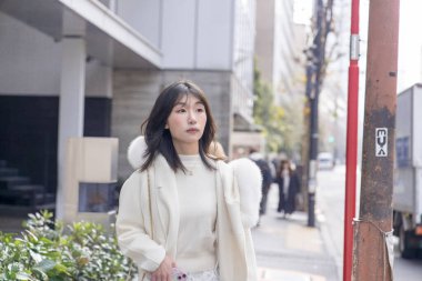 20 'li yaşlarda, siyah saçlı, beyaz önlüklü, tüylü ve beyaz etekli bir Çinli kadın. Minato, Tokyo, Japonya' da halka açık bir yolda yürüyor..