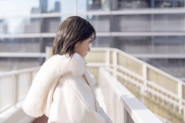 20 'li yaşlarda, siyah saçlı, beyaz önlüklü, tüylü ve beyaz etekli bir Çinli kadın. Minato, Tokyo, Japonya' da halka açık bir yolda yürüyor..