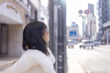 20 'li yaşlarda, siyah saçlı, beyaz önlüklü, tüylü ve beyaz etekli bir Çinli kadın. Minato, Tokyo, Japonya' da halka açık bir yolda yürüyor..