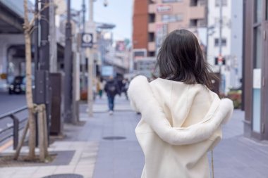 20 'li yaşlarda, siyah saçlı, beyaz önlüklü, tüylü ve beyaz etekli bir Çinli kadın. Minato, Tokyo, Japonya' da halka açık bir yolda yürüyor..
