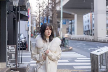 20 'li yaşlarda, siyah saçlı, beyaz önlüklü, tüylü ve beyaz etekli bir Çinli kadın. Minato, Tokyo, Japonya' da halka açık bir yolda yürüyor..