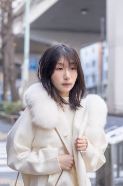 20 'li yaşlarda, siyah saçlı, beyaz önlüklü, tüylü ve beyaz etekli bir Çinli kadın. Minato, Tokyo, Japonya' da halka açık bir yolda yürüyor..