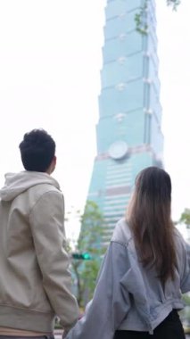 Taipei 'nin Xinyi İlçesi, Taipei İlçesi' nde, arka planda Taipei 101 ile yirmili yaşlarda genç bir Tayvanlı çiftin dikey yavaş çekim videosu var..