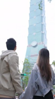 Taipei 'nin Xinyi İlçesi, Taipei İlçesi' nde, arka planda Taipei 101 ile yirmili yaşlarda genç bir Tayvanlı çiftin dikey yavaş çekim videosu var..