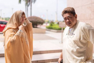 50 'li yaşlardaki Müslüman Malezyalı, beyaz giysili, siyah şapkalı ve krema rengi giyinmiş 30' lu yaşlardaki Çinli kadın Putrajaya, Malezya 'da büyük bir cami önünde namaz kılmaya hazırlanıyor..