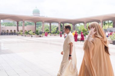 50 'li yaşlardaki Müslüman Malezyalı, beyaz giysili, siyah şapkalı ve krem rengi dini giysileri olan 30' lu yaşlardaki Çinli kadın Putrajaya, Malezya 'da büyük bir camide birlikte yürüyorlar..