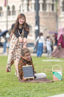 50 'li yaşlarda Malezyalı bir erkek ve 30' lu yaşlarda bir Çinli kadın Malezya 'nın başkenti Kuala Lumpur' da bulunan tarihi binanın önünde karatahtayla fotoğraf çekiyorlar..