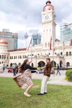 50 'li yaşlarda Malezyalı bir adam ve 30' lu yaşlarda Çinli bir kadın, ikisi de geleneksel Malezya kıyafeti giymiş, Malezya 'nın başkenti Kuala Lumpur' da tarihi bir binanın önünde dans ediyorlar..