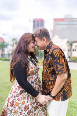 50 'li yaşlarda Malezyalı bir adam ve 30' lu yaşlarda Çinli bir kadın. İkisi de geleneksel Malezya kıyafeti giymiş. Malezya 'nın başkenti Kuala Lumpur' daki tarihi binanın önünde birbirlerinin gözlerinin içine bakıyor..