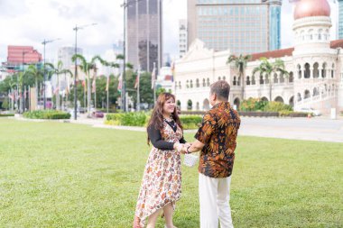 50 'li yaşlarda Malezyalı bir adam ve 30' lu yaşlarda Çinli bir kadın. İkisi de geleneksel Malezya kıyafeti giymiş. Malezya 'nın başkenti Kuala Lumpur' daki tarihi binanın önünde birbirlerinin gözlerinin içine bakıyor..