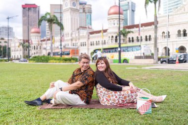 50 'li yaşlarda Malezyalı bir adam ve 30' lu yaşlarda Çinli bir kadın. İkisi de Malezya 'nın başkenti Kuala Lumpur' da bulunan tarihi bir binanın önündeki çimlerin üzerinde oturuyorlar..