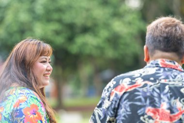 50 'li yaşlarda Malezyalı bir adam ve 30' lu yaşlarında Çinli bir kadın, ikisi de renkli giyinmiş, yakın bir bankta oturuyor ve Malezya 'nın Kuala Lumpur kentindeki KLCC Parkı' nda birlikte yürüyorlar..