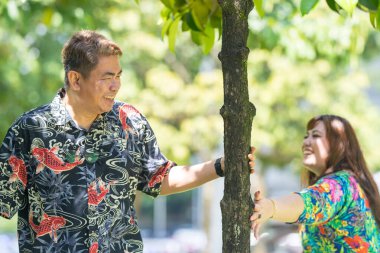 50 'li yaşlarında Malezyalı bir adam renkli gömlek giyiyor ve 30' lu yaşlarında Çinli bir kadın Malezya, Kuala Lumpur 'daki KLCC Parkı' nda ağaçların gölgesinde kovalamaca oynuyor..