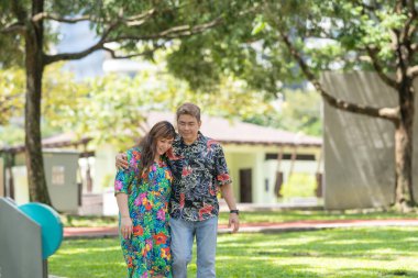 50 'li yaşlarda Malezyalı bir adam renkli gömlek giyiyor ve 30' lu yaşlarında Çinli bir kadın Malezya 'nın Kuala Lumpur kentindeki KLCC Parkı' nda birlikte yürüyor..