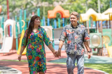 50 'li yaşlarda Malezyalı bir adam renkli gömlek giyiyor ve 30' lu yaşlarında Çinli bir kadın Malezya 'nın Kuala Lumpur kentindeki KLCC Parkı' nda birlikte yürüyor..