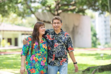 50 'li yaşlarda Malezyalı bir adam renkli gömlek giyiyor ve 30' lu yaşlarında Çinli bir kadın Malezya 'nın Kuala Lumpur kentindeki KLCC Parkı' nda birlikte yürüyor..