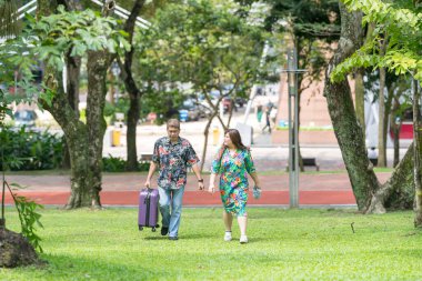 50 'li yaşlarda Malezyalı bir adam renkli gömlek giyiyor ve 30' lu yaşlarında Çinli bir kadın Malezya 'nın Kuala Lumpur kentindeki KLCC Parkı' nda birlikte yürüyor..