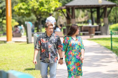 50 'li yaşlarda Malezyalı bir adam renkli gömlek giyiyor ve 30' lu yaşlarında Çinli bir kadın Malezya 'nın Kuala Lumpur kentindeki KLCC Parkı' nda birlikte yürüyor..