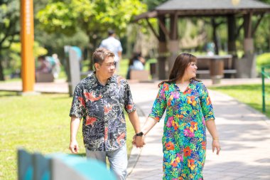 50 'li yaşlarda Malezyalı bir adam renkli gömlek giyiyor ve 30' lu yaşlarında Çinli bir kadın Malezya 'nın Kuala Lumpur kentindeki KLCC Parkı' nda birlikte yürüyor..