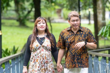 50 'li yaşlarında Malezyalı bir adam geleneksel 30' lu yaşlarda geleneksel elbiseler giyen Çinli bir kadın, Kuala Lumpur 'daki Botani Perdana Köprüsü' nde birlikte vakit geçiriyorlar.