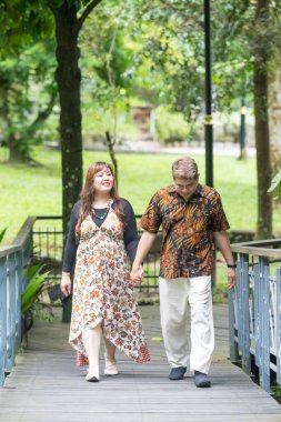 50 'li yaşlarında Malezyalı bir adam geleneksel 30' lu yaşlarda geleneksel elbiseler giyen Çinli bir kadın, Kuala Lumpur 'daki Botani Perdana Köprüsü' nde birlikte vakit geçiriyorlar.