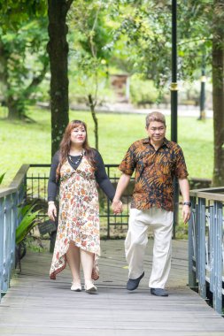 50 'li yaşlarında Malezyalı bir adam geleneksel 30' lu yaşlarda geleneksel elbiseler giyen Çinli bir kadın, Kuala Lumpur 'daki Botani Perdana Köprüsü' nde birlikte vakit geçiriyorlar.