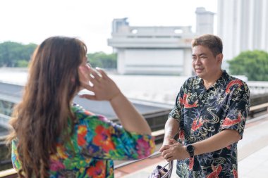 50 'li yaşlarında Malezyalı bir adam renkli gömlek giyiyor ve 30' lu yaşlarında Çinli bir kadın renkli elbiseler giyiyor. Kuala Lumpur, Malezya 'da bir tren istasyonunda birlikte vakit geçiriyorlar..