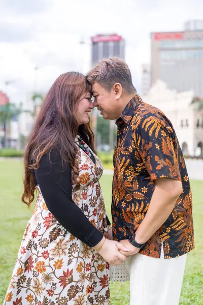 50 'li yaşlarda Malezyalı bir adam ve 30' lu yaşlarda Çinli bir kadın. İkisi de geleneksel Malezya kıyafeti giymiş. Malezya 'nın başkenti Kuala Lumpur' daki tarihi binanın önünde birbirlerinin gözlerinin içine bakıyor..