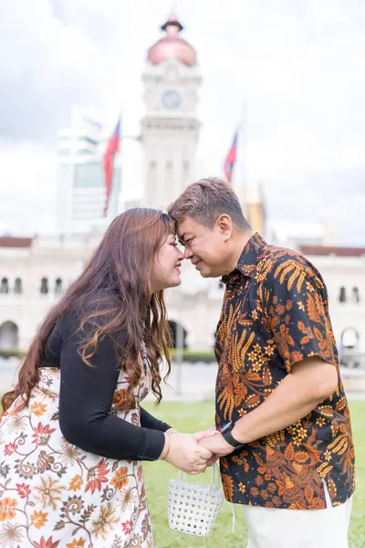 50 'li yaşlarda Malezyalı bir adam ve 30' lu yaşlarda Çinli bir kadın. İkisi de geleneksel Malezya kıyafeti giymiş. Malezya 'nın başkenti Kuala Lumpur' daki tarihi binanın önünde birbirlerinin gözlerinin içine bakıyor..